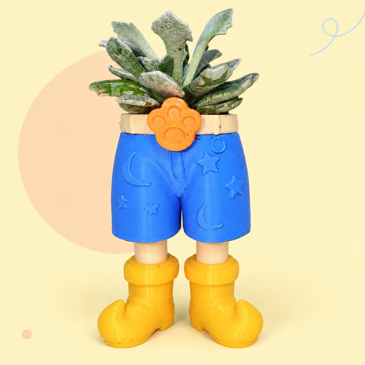 Blue shorts planter with stars and crescent moons, a cream belt, orange paw buckle, yellow boots and a succulent